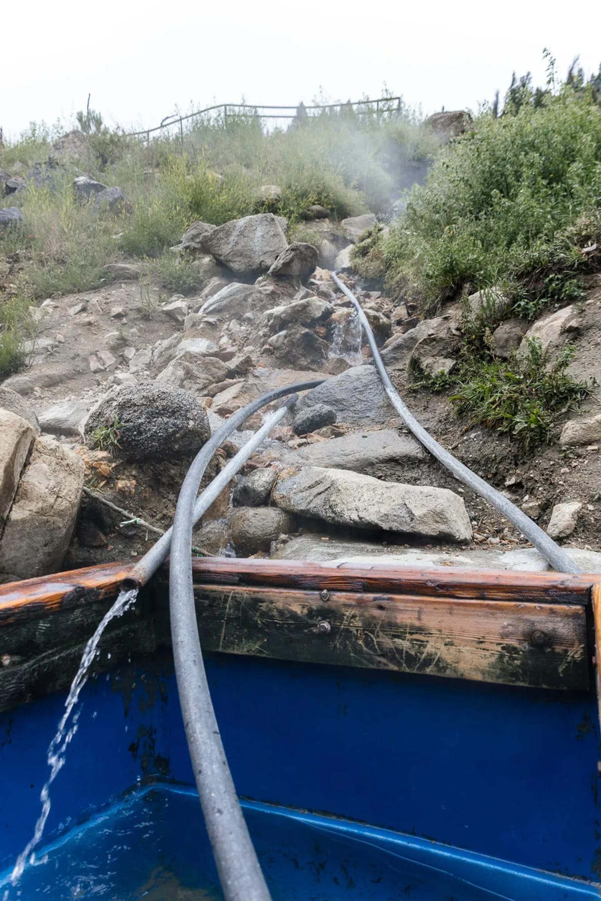 Several pipes run down the hill at Sunbeam Hot Springs into a large blue tub